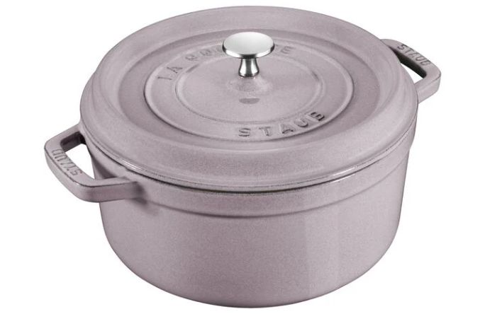 A round, lavender-colored cast iron Dutch oven with a silver knob on the lid, featuring side handles.